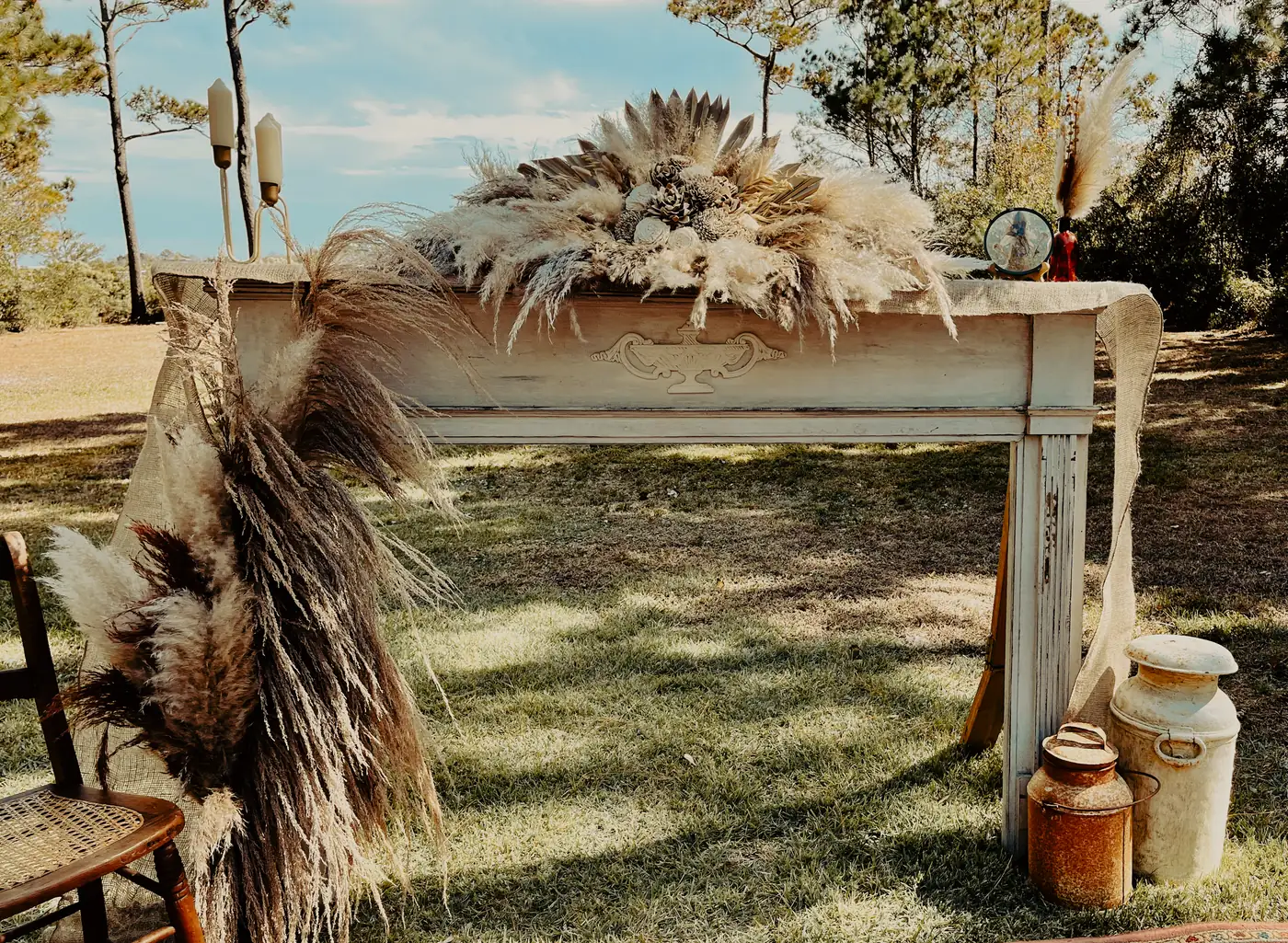Vintage fireplace mantel styled with pampas grass, candlesticks, and rustic details at an outdoor celebration